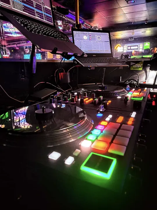 Beleuchtete DJ-Decks, Plattenspieler und Laptops in einem Club