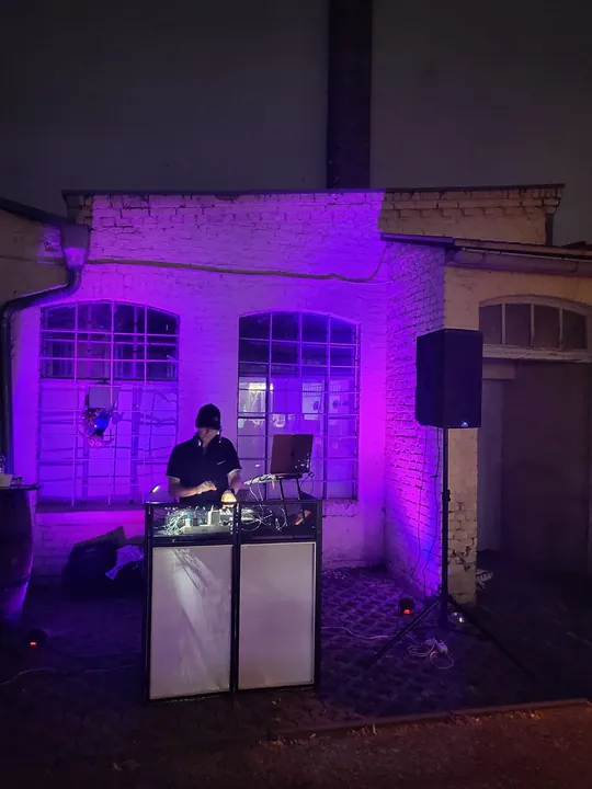 Ramón am DJ-Pult vor einer violett beleuchteten Gebäudefassade