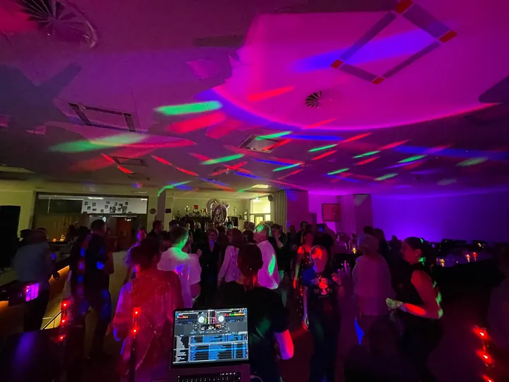 Volle Tanzfläche mit farbigem Partylicht, aufgenommen vom DJ-Pult