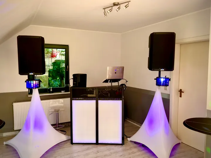 Weißes DJ-Pult zwischen zwei Lautsprechern in einer hellen Location