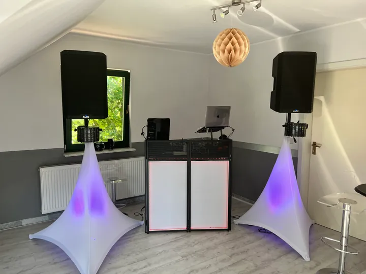 DJ-Pult mit beleuchteten Lautsprecherstativen und festlicher Raumdekoration