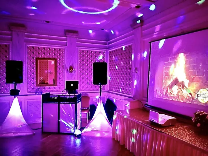 DJ-Pult, Lichtanlage und große Leinwand in einem beleuchteten Festsaal